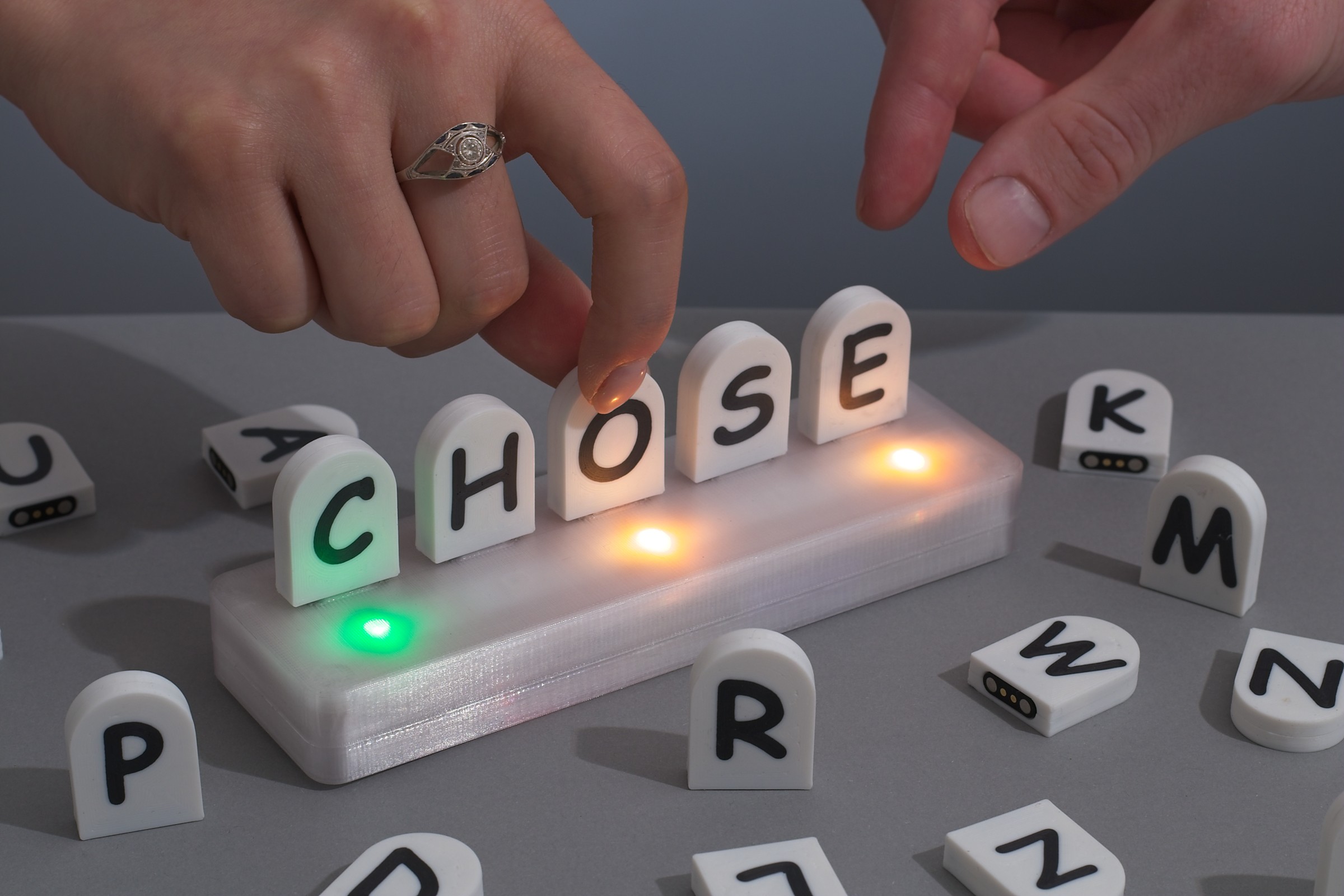 Hands arranging illuminated Tactle letter tiles to spell CHOSE